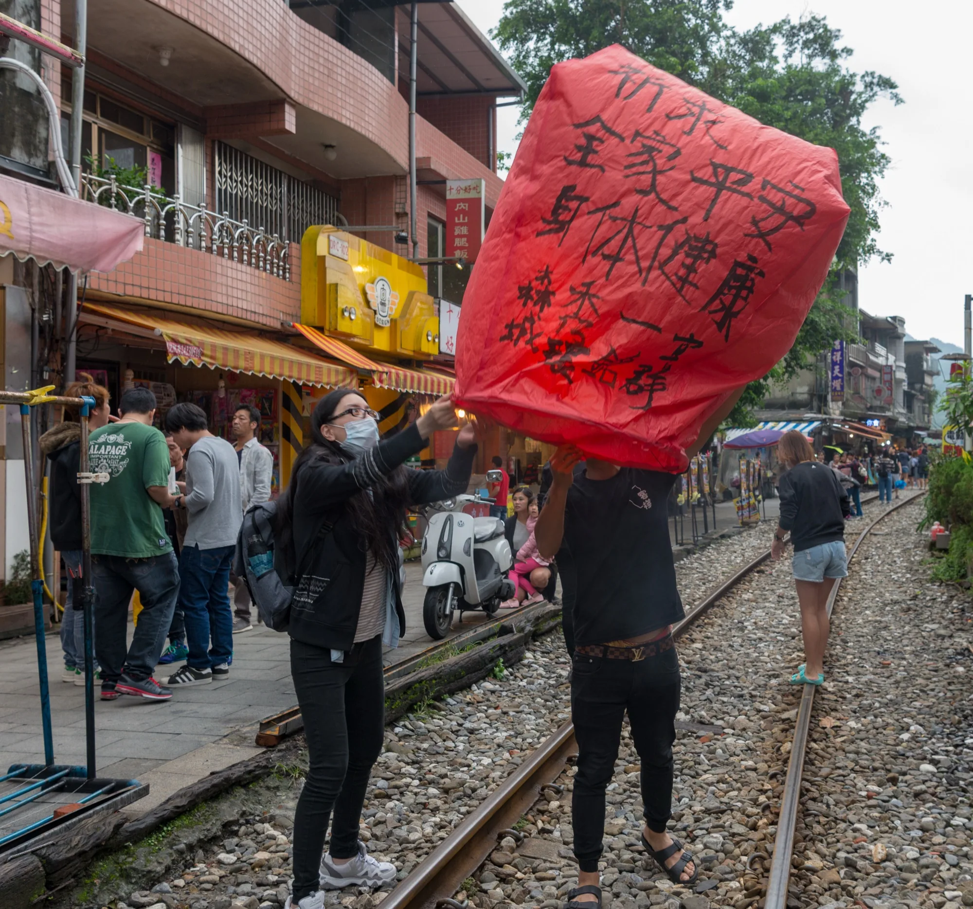 十分老街白天場景，平溪線鐵道穿過老街中央，兩側天燈攤位與店面林立