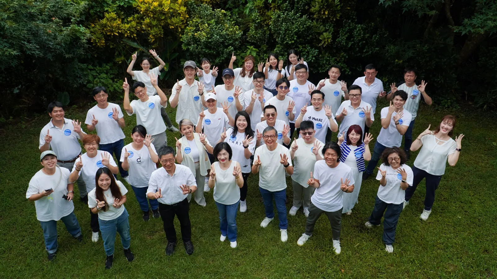 AAMA台北揺籃プログラム第14期メンターと起業家の屋外集合写真、白いAAMA記念Tシャツを着用し、背景は草地と森林
