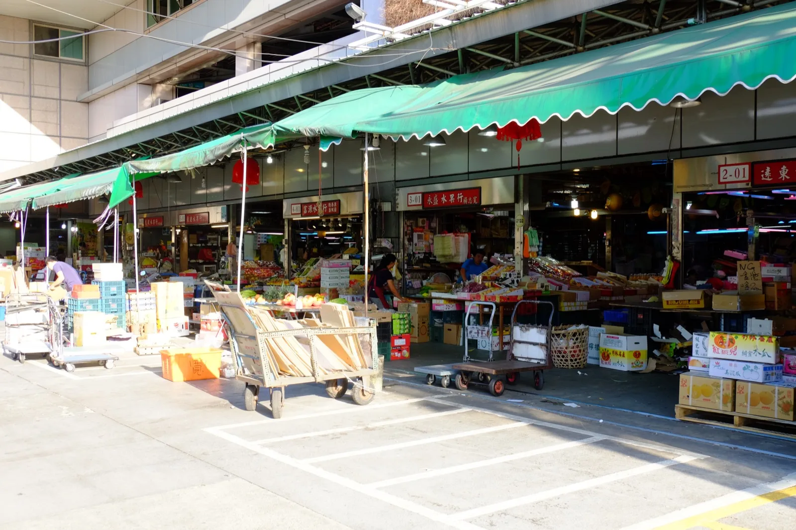 Os estabelecimentos de frutas no primeiro andar do Mercado Binjiang, caixas de madeira empilhadas, letreiros por toda parte, um funcionário se move entre os corredores