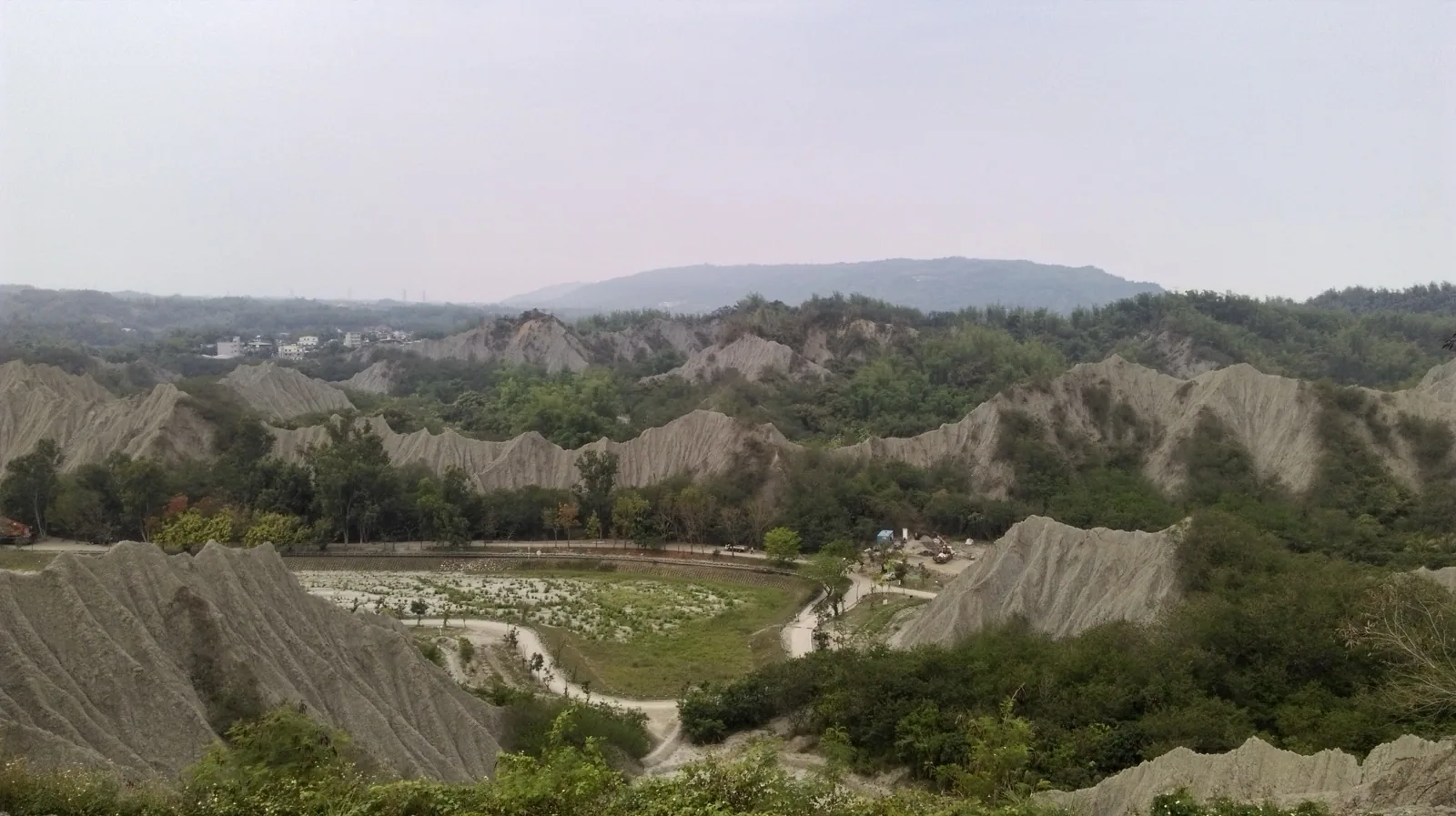 高雄古亭坑層的泥岩惡地,灰白色的山脊一道道裸露、幾乎寸草不生,遠方是稀疏的綠樹與小聚落