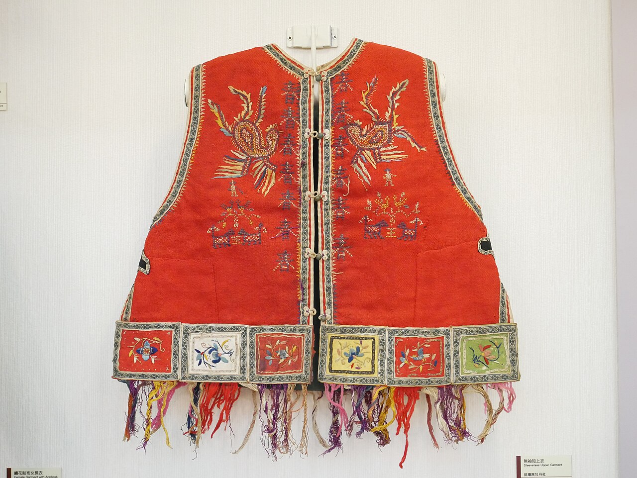 排灣族牡丹社傳統無袖短上衣，紅底刺繡。1956 年國立臺灣大學典藏入庫，是 1874 年牡丹社事件當代的物質證據之一。