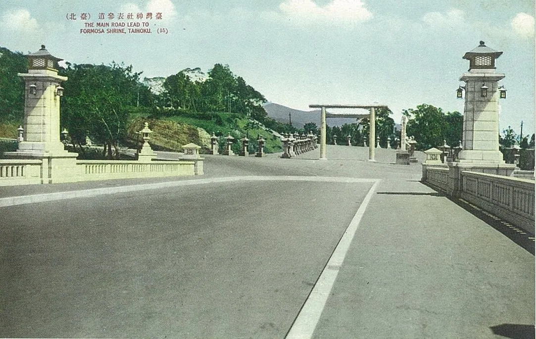 Vue de l'approche du sanctuaire de Taiwan (Chokushi Kaidō) durant la période coloniale japonaise, montrant le pont Meiji et l'entrée du sanctuaire au loin, avec un torii et une allée arborée. Cette route cérémonielle de cinq kilomètres fut élargie en une avenue à cinq voies de 40 mètres entre 1937 et 1941