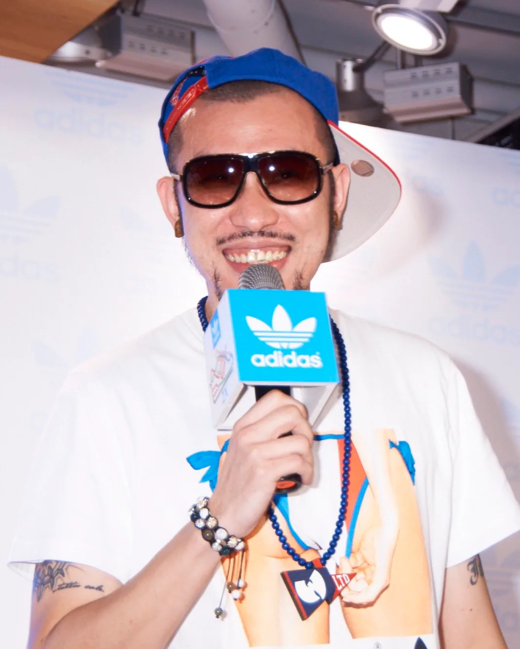 Rapper MC HotDog performing onstage in profile while holding an adidas microphone, wearing a cap, with a focused expression.