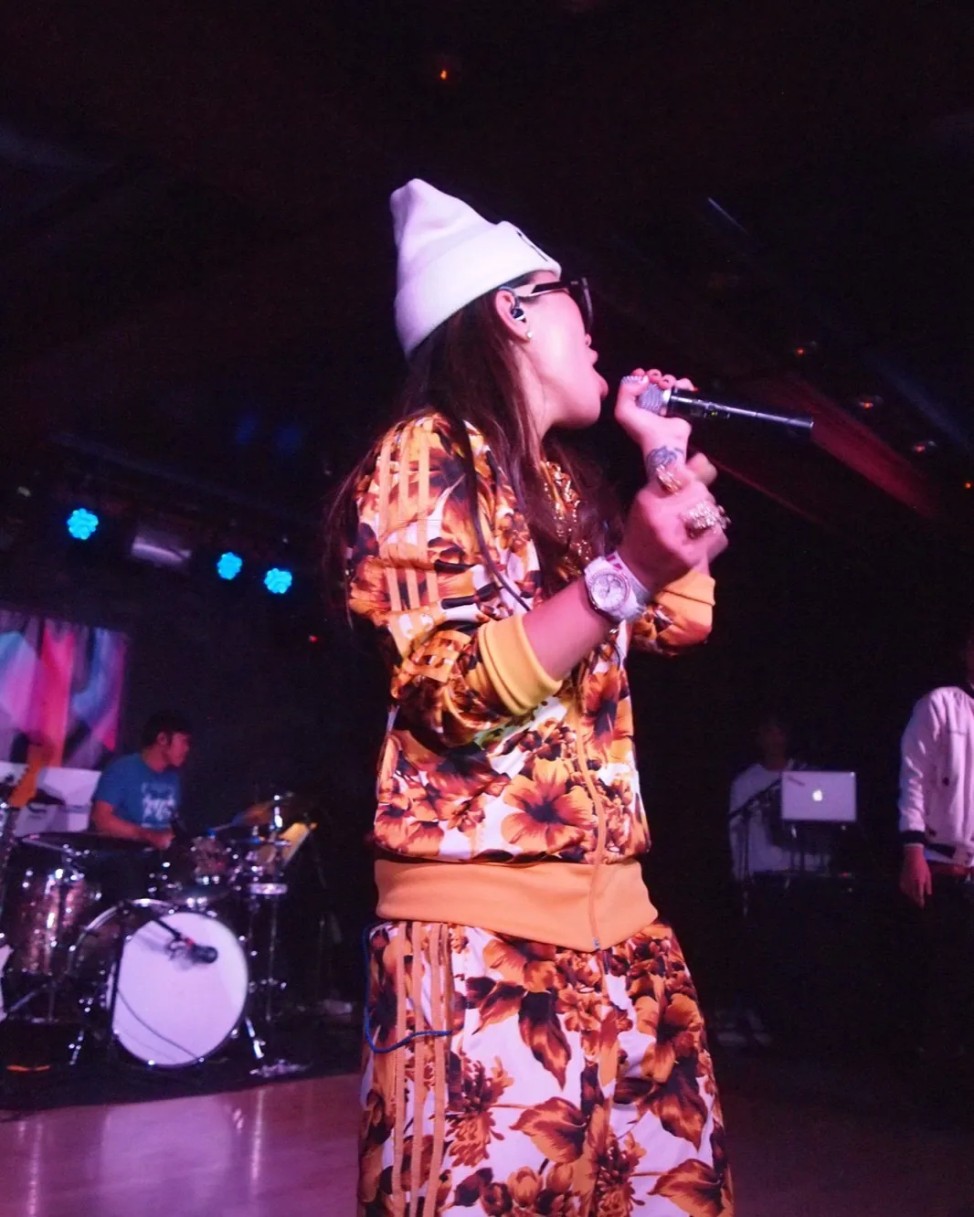 Rapper Miss Ko performing live with a microphone, long-haired and confident in expression.