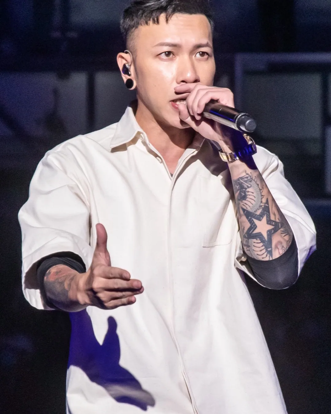 MJ116 member Kenzy (Chou Wen-chieh) performing at a Taoyuan City Government event, wearing a hat and holding a microphone.