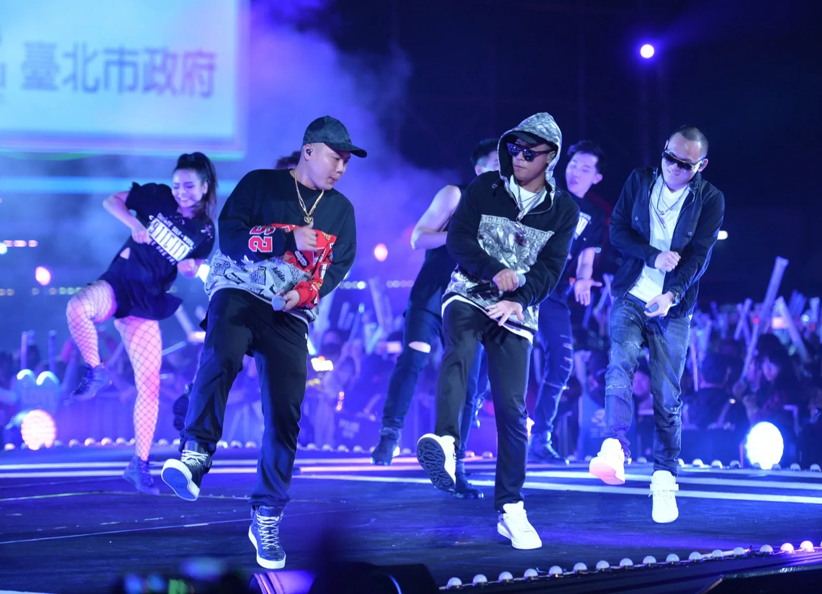 Nine One One performing on the large stage of Taipei's New Year's Eve concert: the three hold microphones, with the city night sky and stage lights in the background.
