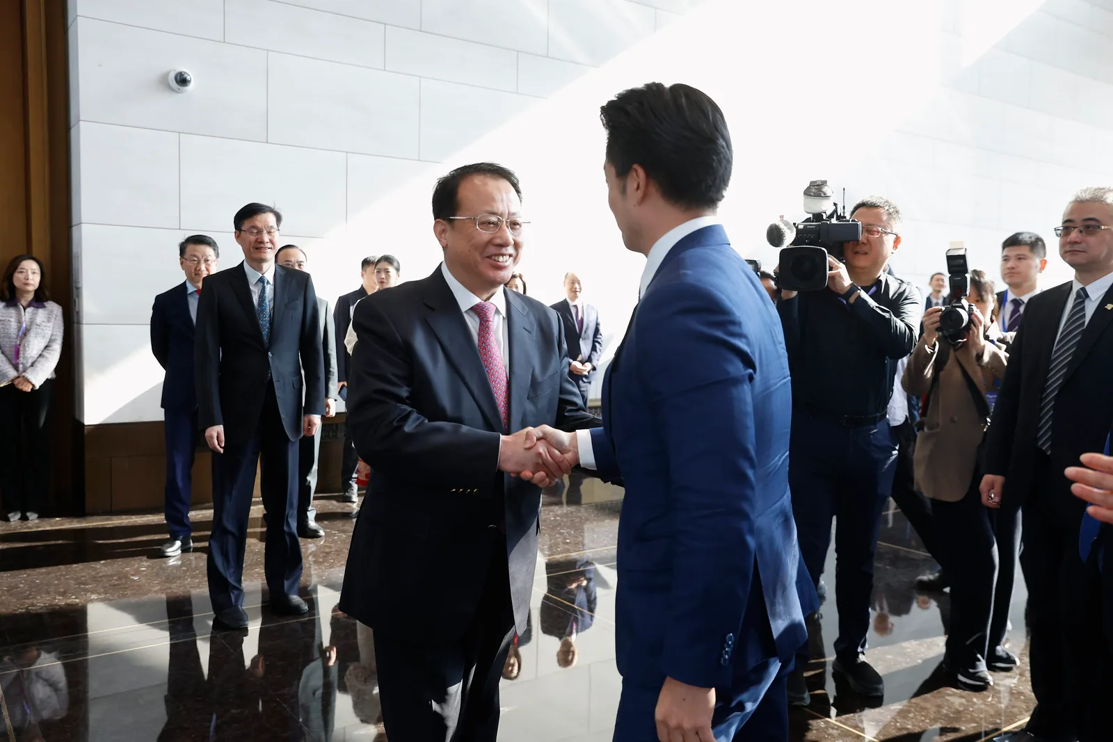 Am 28. Dezember 2025 schüttelt Chiang Wan-an dem Shanghaier Bürgermeister Gong Zheng in der Halle die Hand, flankiert von Begleitbeamten, im Hintergrund stehen Pressefotografen