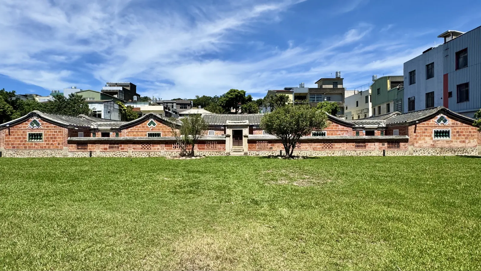 新竹新埔的潘屋建築群,紅磚與馬背山牆在天光下延展。杜潘芳格 1927 年出生於新埔客家望族,這座家族地景是她童年與跨語 generational 記憶的物質錨點。
