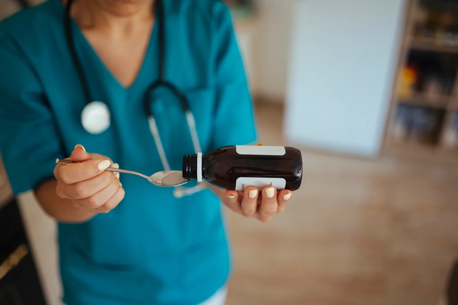 Enfermeira de uniforme médico em um quarto brilhante, segurando uma colher pronta para alimentar o paciente com medicamento líquido, detalhe próximo do ato de cuidado íntimo