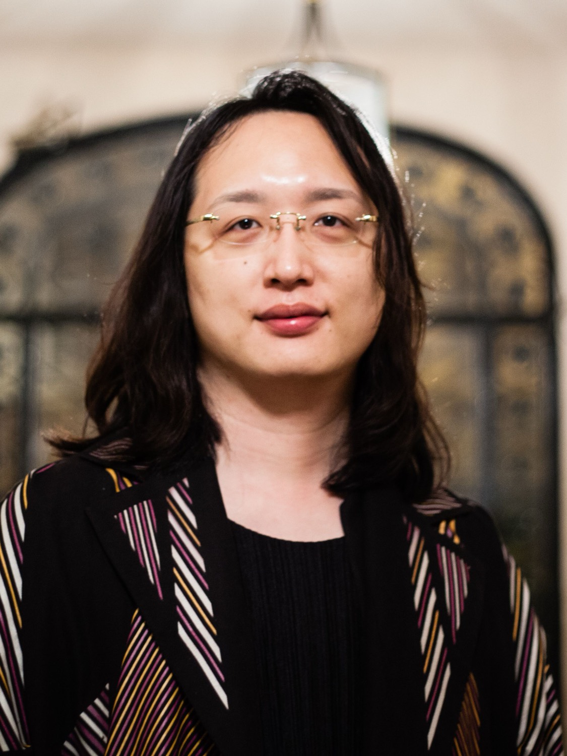 唐鳳的個人肖像,戴細框眼鏡、留短髮、面帶微笑,背景單純的淺色。