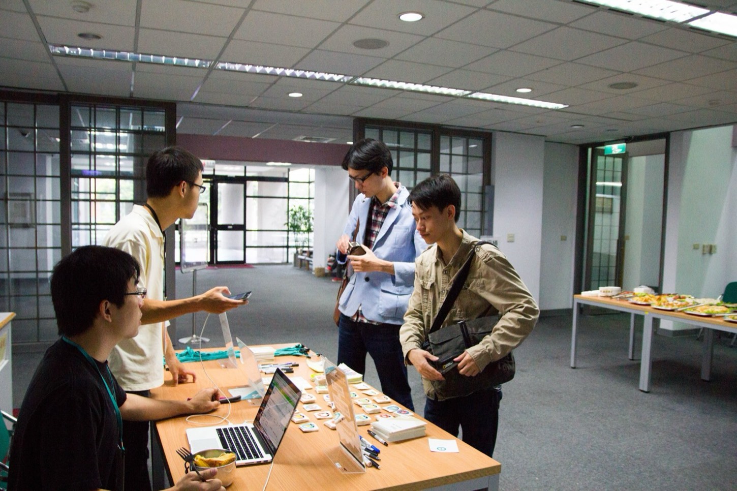 一群人圍坐在長桌前協作,筆電與螢幕亮著,這是 2015 年 g0v 第十三次黑客松的室內現場,參與者分組投入公民科技專案。