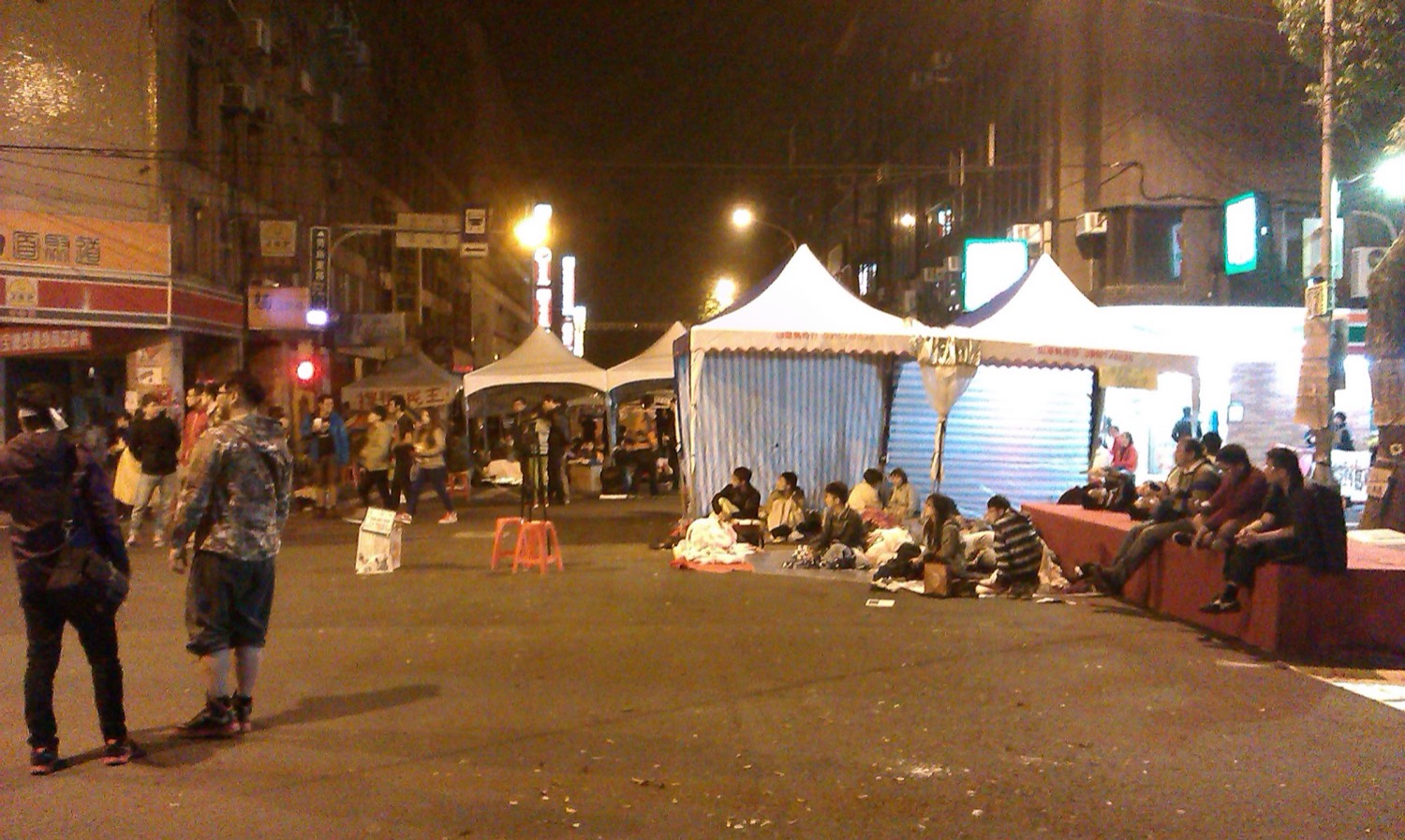 太陽花學運期間的台北街頭,立法院周邊聚集人群與抗議布條,地面靜置一片運動現場的氛圍。