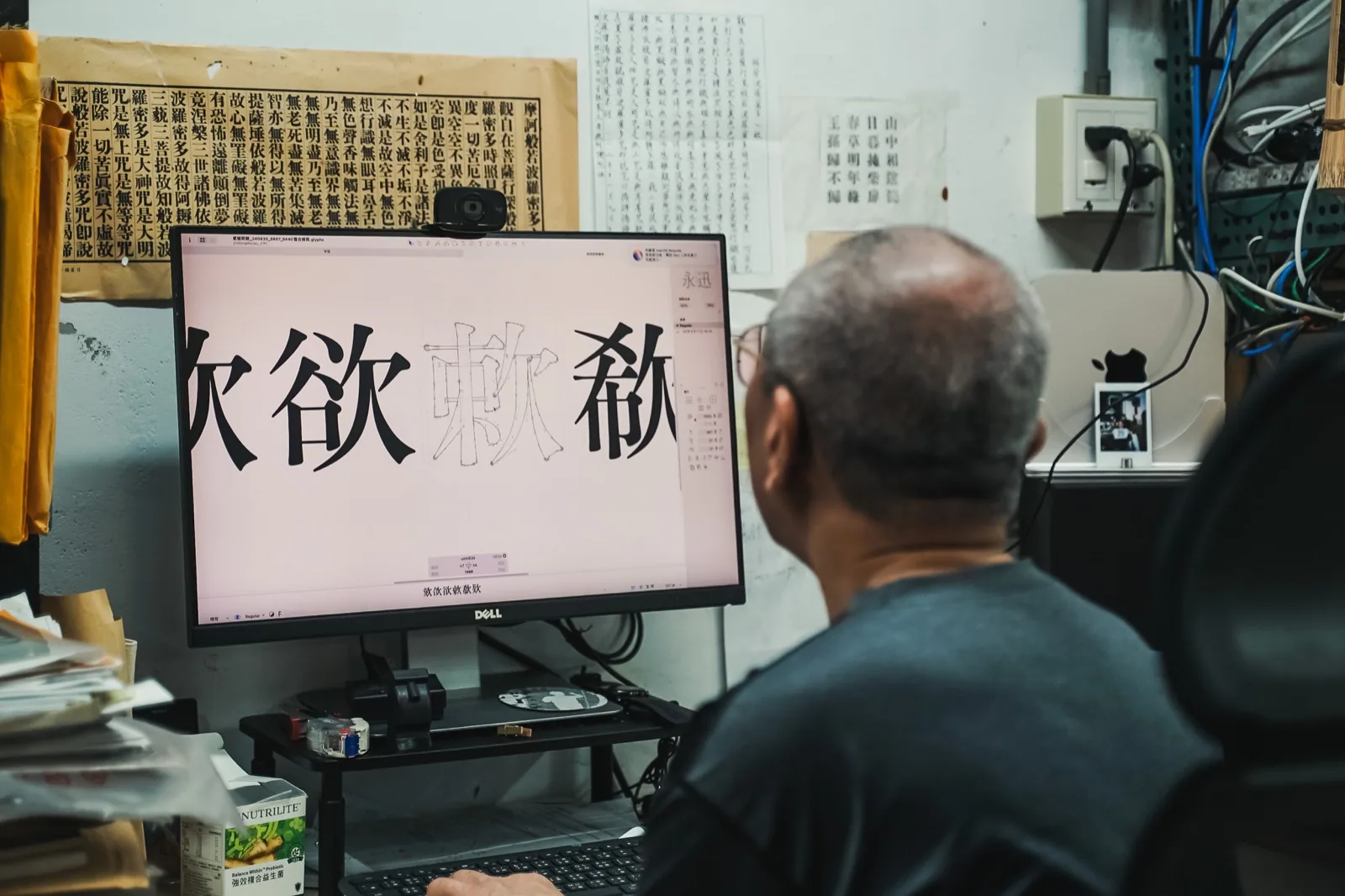 日星鑄字行張介冠坐在螢幕前修整數位化的鉛字字形,身後牆上掛滿密密麻麻的鉛字字樣表